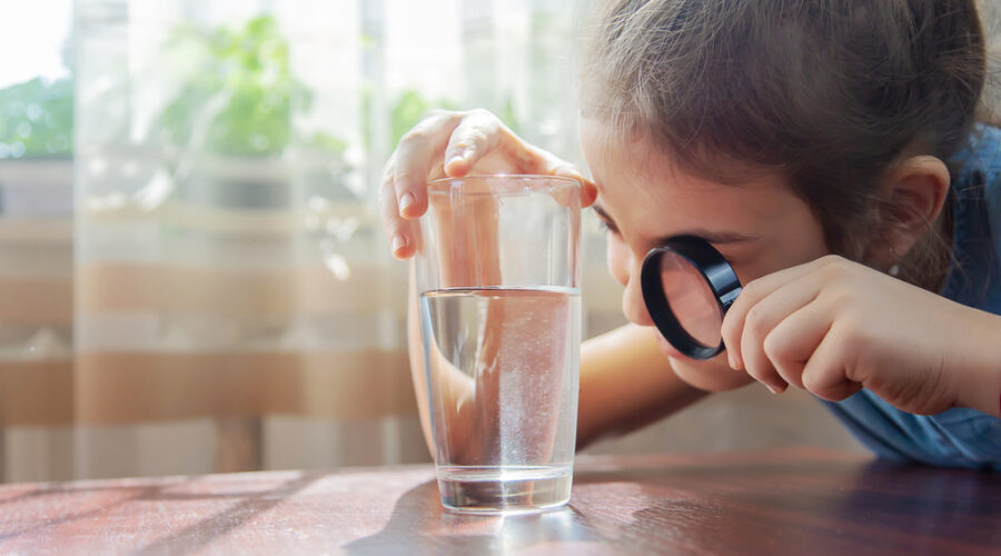 Child inspecting a glass of water with a magnifying glass.